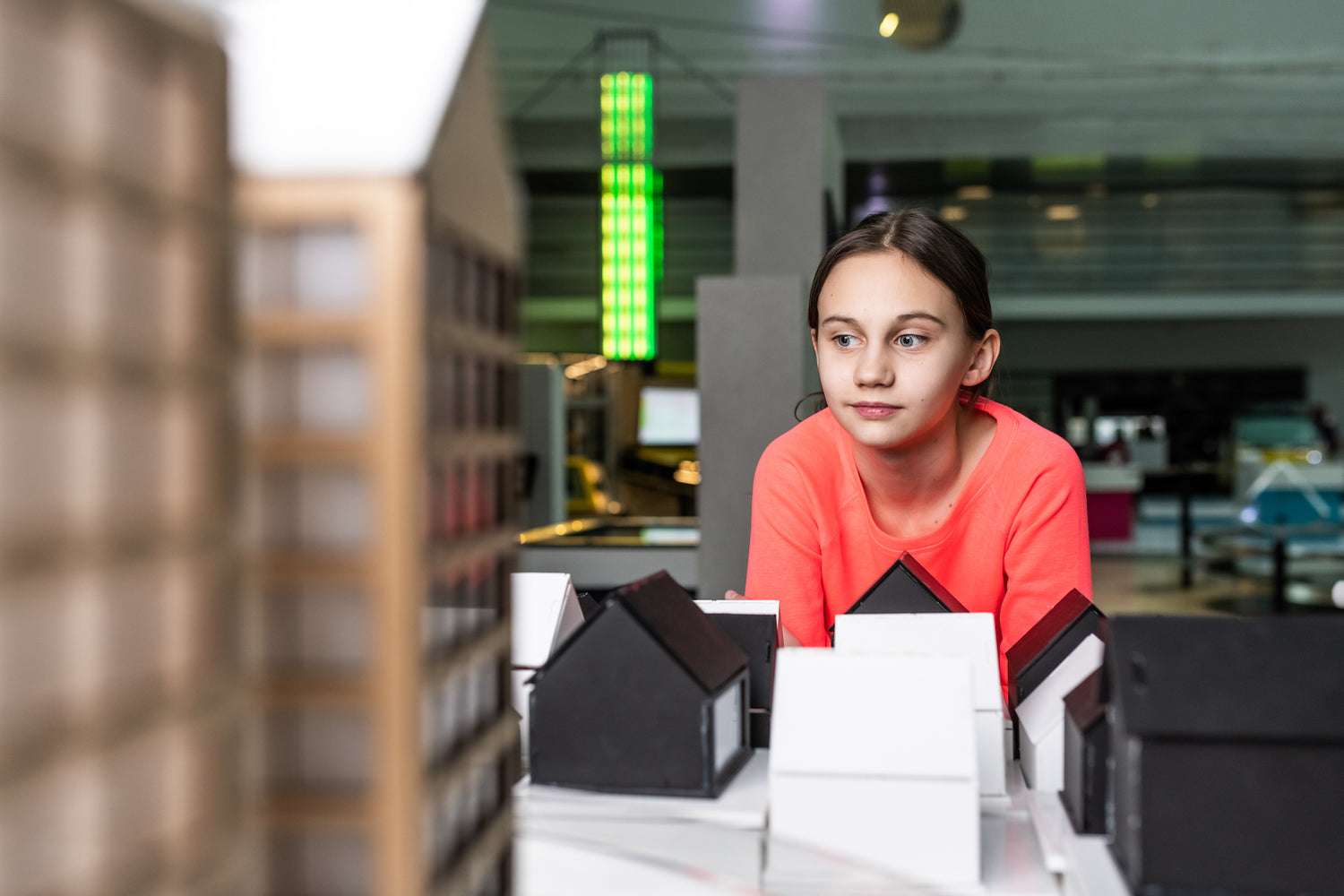 In the Heureka Electricity exhibition, a girl wearing a coral-colored shirt looks curiously at a wooden city structure.
