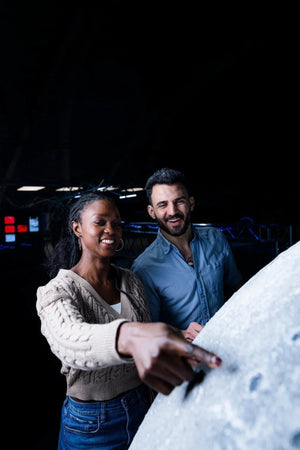 Heurekan Matkalla avaruudessa -näyttelyssä nainen osoittaa sormella suuren Kuun pintaan. Mies katsoo vierestä. 