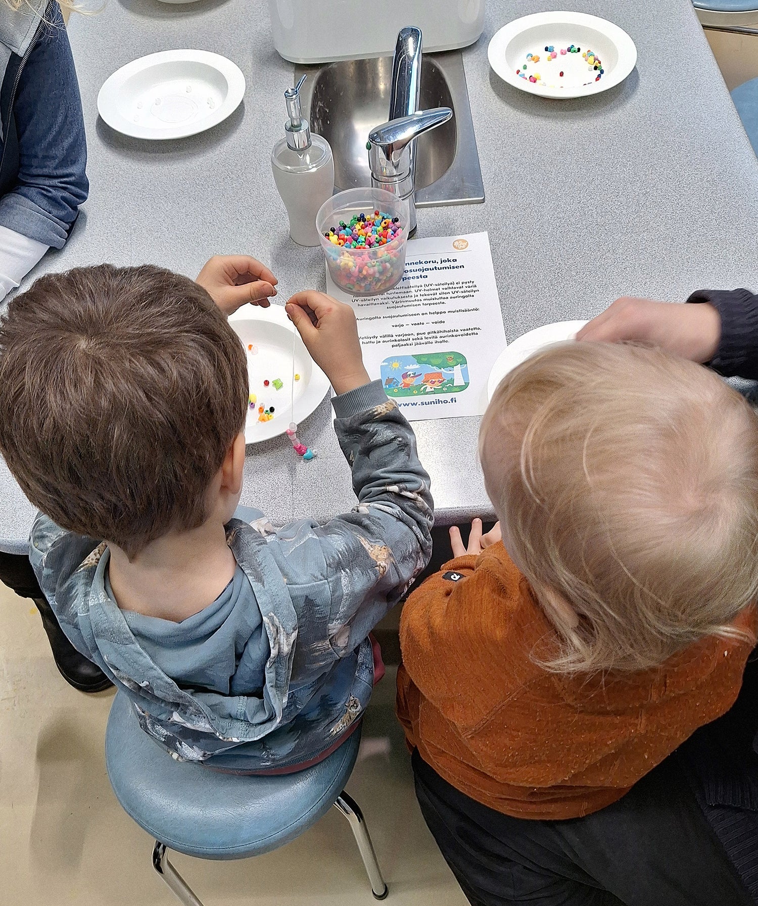 Kaksi lasta askartelevat UV-rannekoruja.