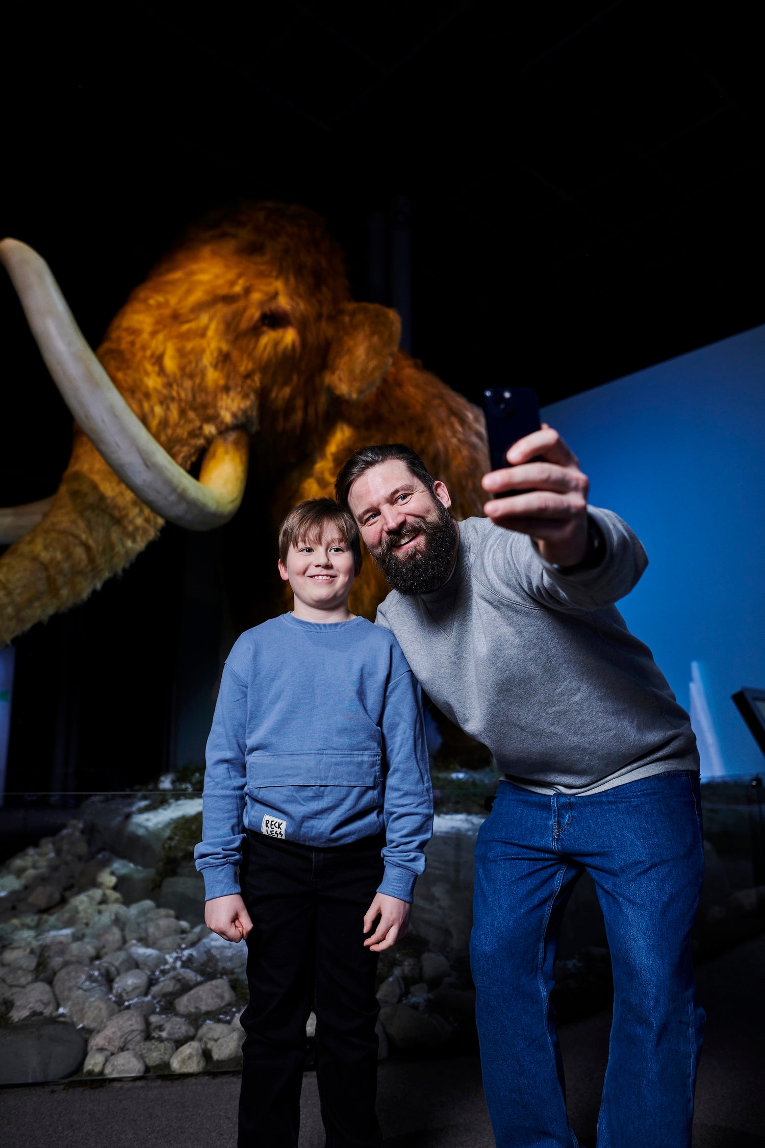 Mies ja poika ottavat selfien mammutin edessä.