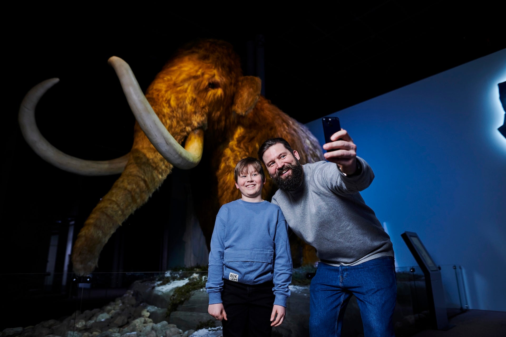 A boy and a man in front of a mammoth at the Giants of the Ice Age exhibition.