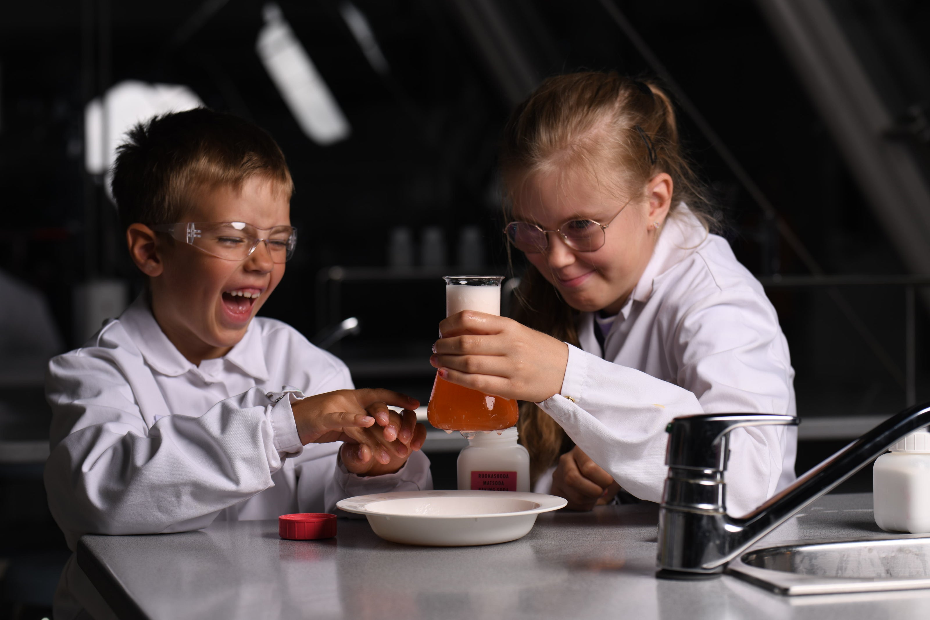 Tyttö ja poika tekevät kokeiluja Heurekan laboratoriossa. Poikaa naurattaa kovasti. 