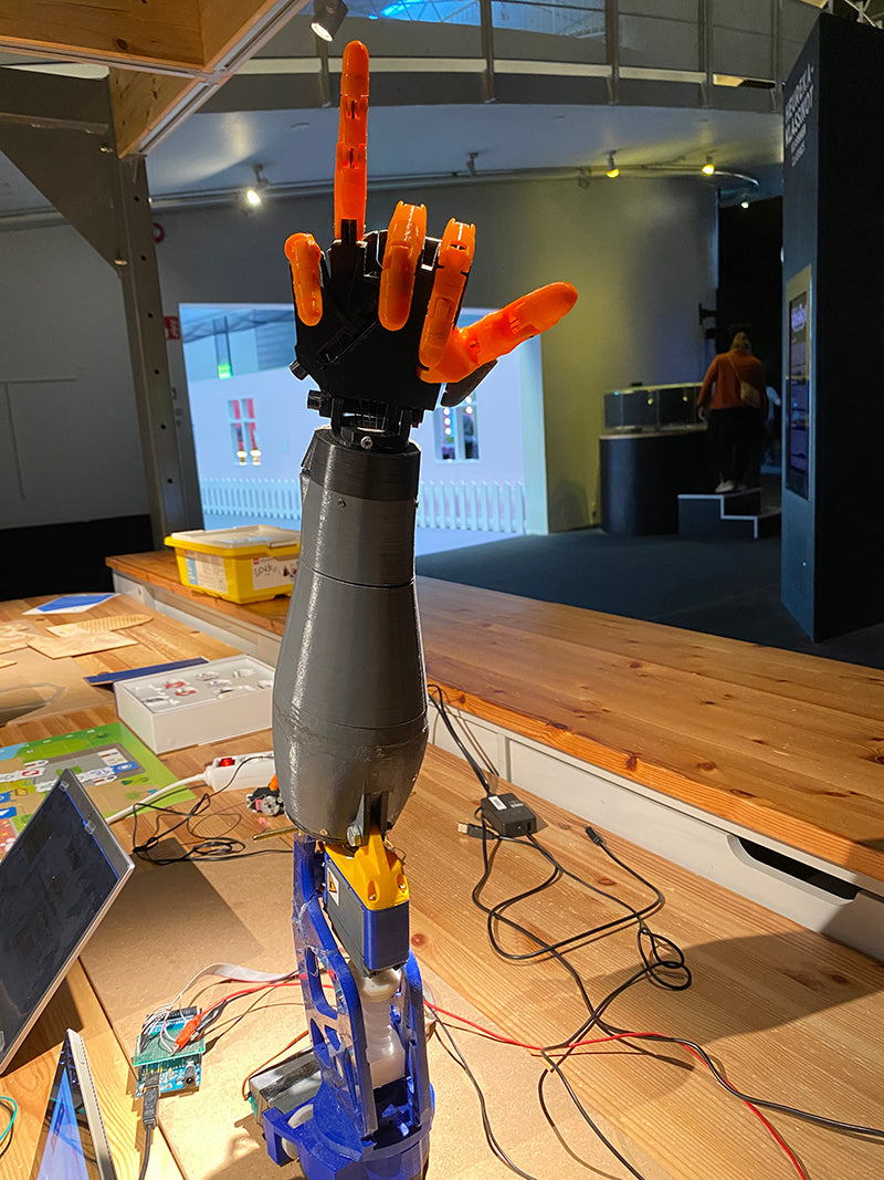 Harmaa ja musta robottikäsi, jolla on oranssit sormet.