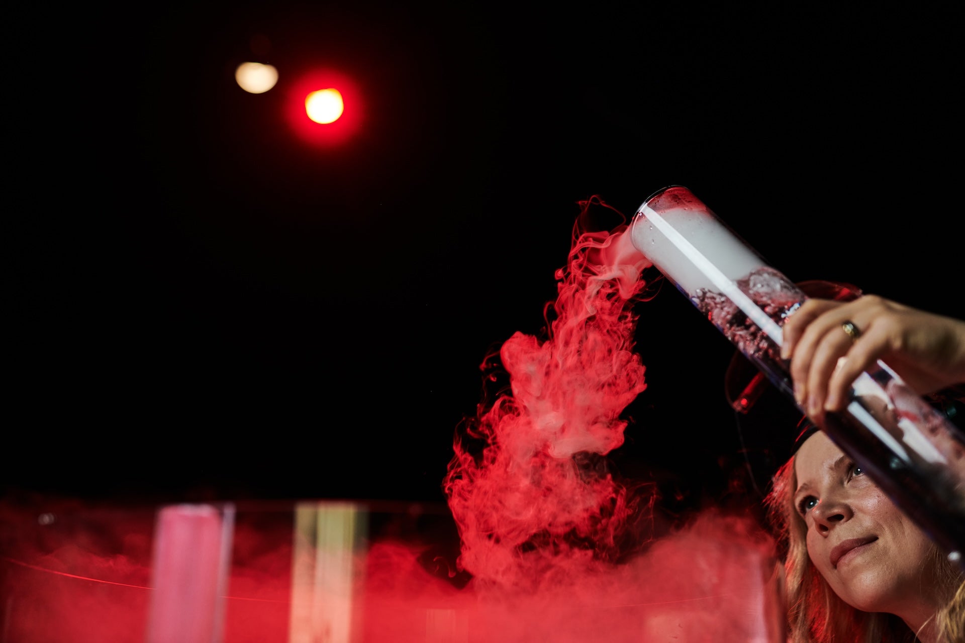 Innoittaja kaataa koeputkesta savua, joka näyttää valossa punaiselta.